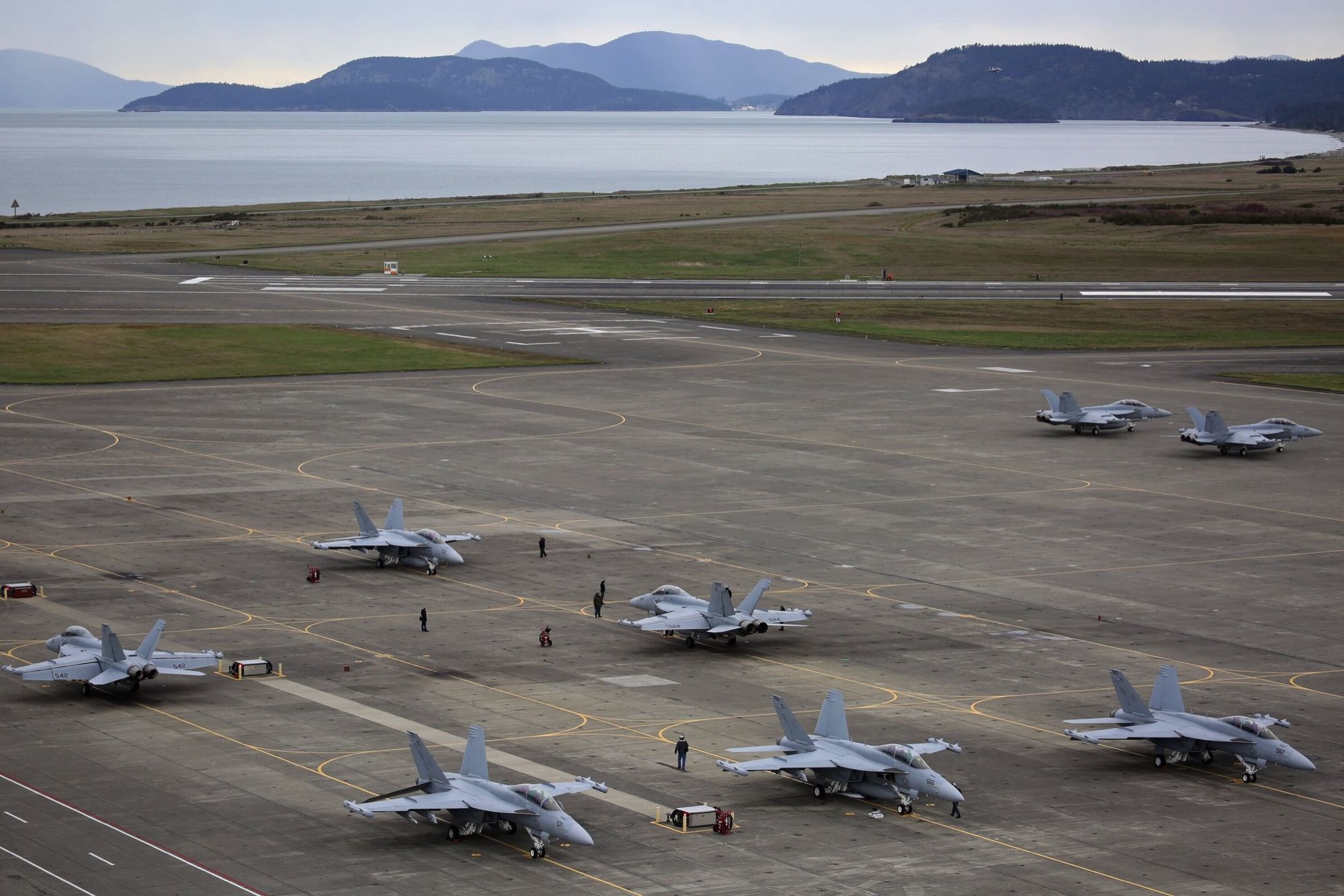 EA-18G Growler aircraft parked on the apron of a coastal naval air station, with runways and taxiways across the airfield.